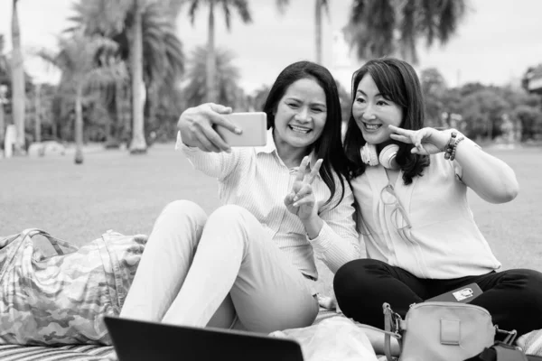 Two mature Asian women taking selfie at park with mobile phone — Stock Photo, Image