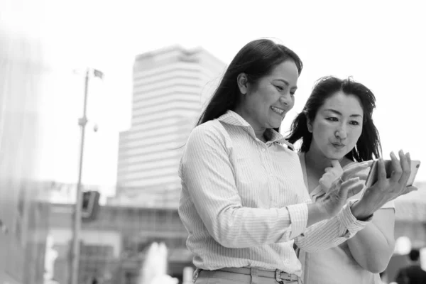 Twee volwassen Aziatische vrouwen samen buiten het winkelcentrum in Bangkok stad met behulp van telefoon — Stockfoto