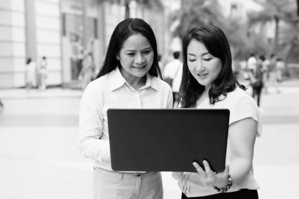 Twee volwassen Aziatische vrouwen met behulp van laptop computer buiten — Stockfoto