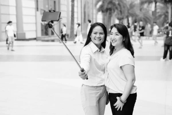Dos mujeres asiáticas tomando selfie usando selfie stick al aire libre —  Fotos de Stock