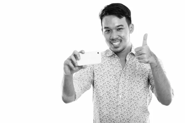 Pemuda Asia yang bahagia tersenyum sambil mengambil gambar dengan ponsel dan memberikan jempol ke atas — Stok Foto