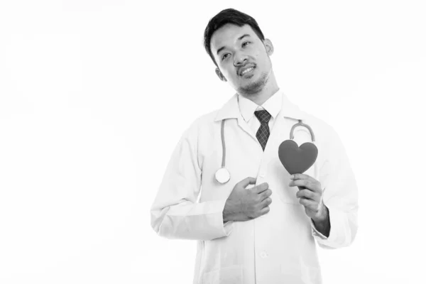 Студийный снимок молодого азиатского врача, держащего красное сердце, думая: — стоковое фото