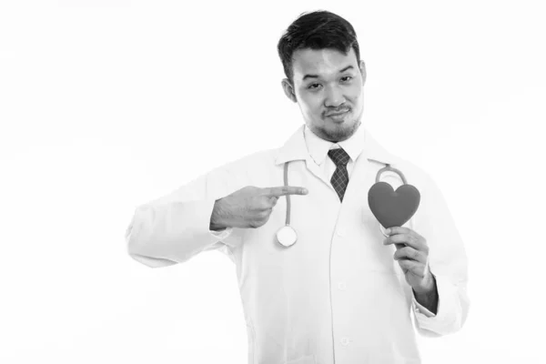 Студийный снимок молодого азиатского врача, держащего и указывающего на красное сердце — стоковое фото