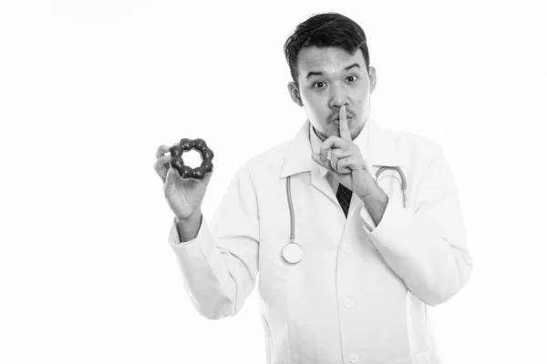 Studio shot van jonge Aziatische man arts houden donut met vinger op de lippen — Stockfoto