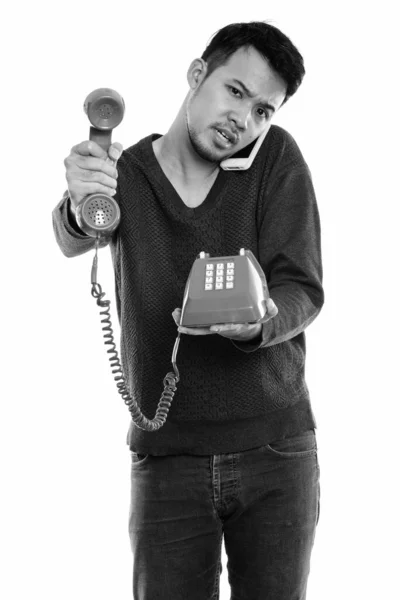 Studio shot dari pemuda Asia berdiri dan memberikan telepon lama sambil berbicara di telepon genggam — Stok Foto