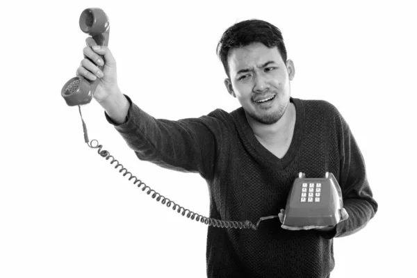 Studio záběr mladého asijského muže drží starý telefon vypadá rozrušeně — Stock fotografie