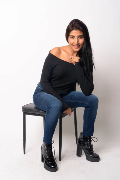 Full body shot di felice giovane donna persiana sorridente e seduta sulla sedia — Foto Stock