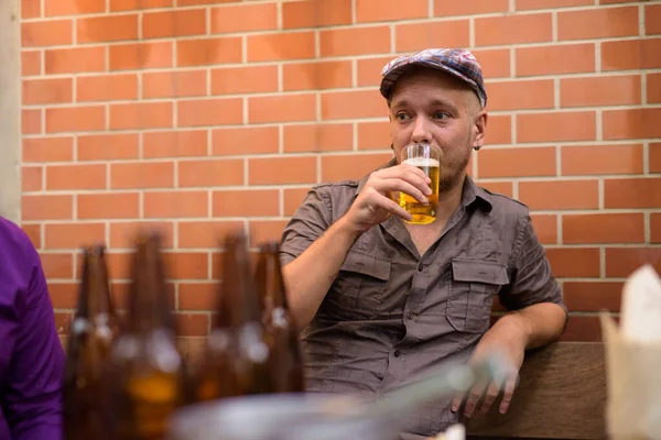 Happy hipster man sitting outdoors and drinking beer