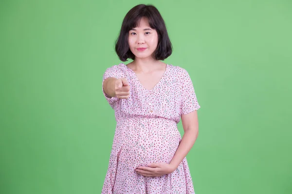 Портрет красивой азиатской беременной женщины, указывающей на камеру — стоковое фото
