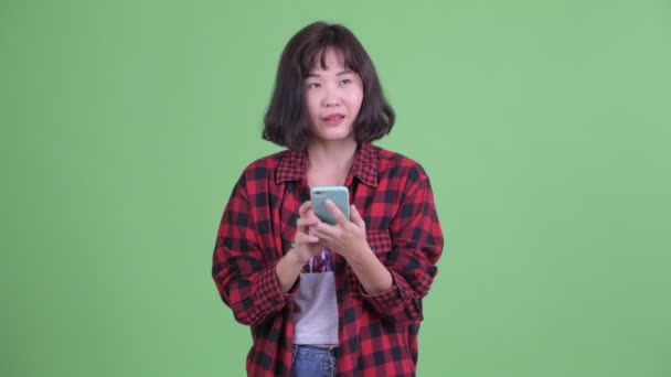 Ευτυχισμένη ασιατική hipster γυναίκα σκέφτεται κατά τη χρήση του τηλεφώνου — Αρχείο Βίντεο