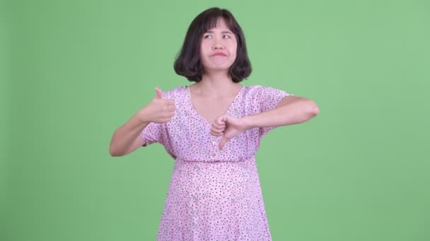 Confused Asian pregnant woman choosing between thumbs up and thumbs down — Stock Video