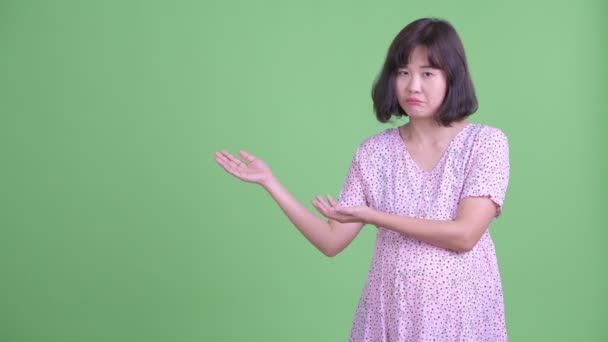 Stressed Asian pregnant woman showing something and giving thumbs down — Stock Video