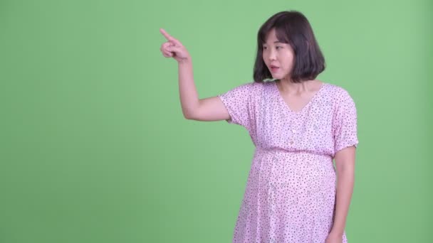 Mutlu Asyalı hamile kadın bir şeye dokunuyor ve şaşırmış görünüyor. — Stok video