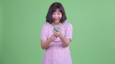 Mutlu Asyalı hamile kadın telefonu kullanıyor ve iyi haberler alıyor.