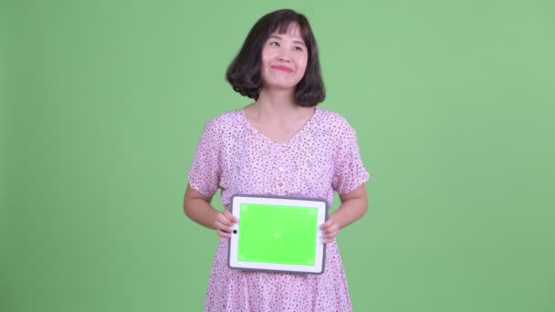 Mulher grávida asiática feliz pensando ao mostrar tablet digital — Vídeo de Stock