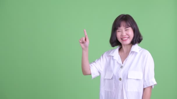 Happy beautiful Asian businesswoman talking while pointing up — Stock Video