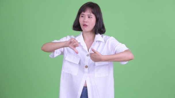 Confused Asian businesswoman choosing between thumbs up and thumbs down — Stok video