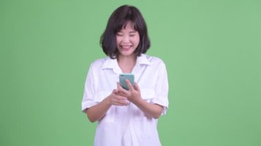 Mutlu Asyalı iş kadını telefonu kullanıyor ve iyi haberler alıyor.