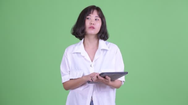 Happy beautiful Asian businesswoman thinking while using digital tablet — Stock Video