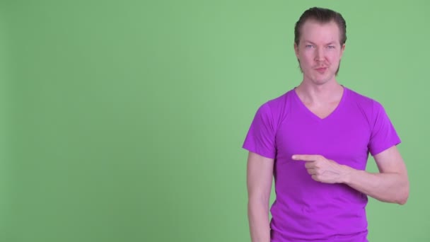Glücklicher junger gutaussehender Mann zeigt mit dem Finger und gibt die Daumen nach oben — Stockvideo