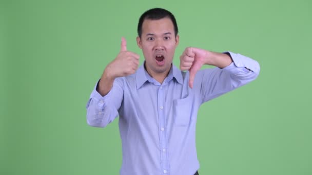 Confused Asian businessman choosing between thumbs up and thumbs down — Stock Video