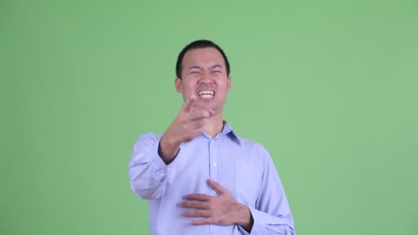 Студийный кадр счастливого азиатского бизнесмена, смеющегося и указывающего на камеру — стоковое видео