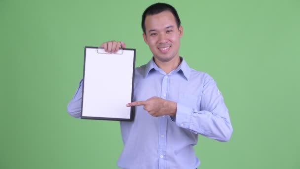 Щасливий азіатський бізнесмен, який показує дошку з автоматом і віддає пальці вгору. — стокове відео