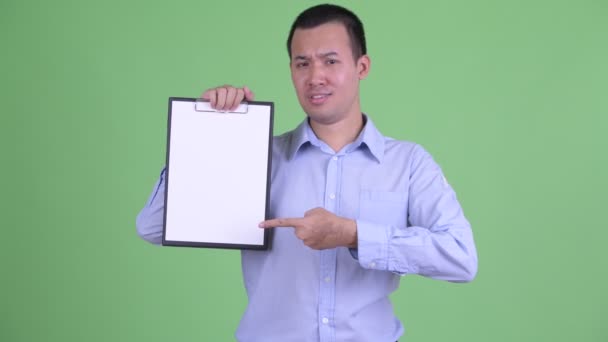 Gespannen aziatische zakenman tonen klembord en het geven van duimen naar beneden — Stockvideo