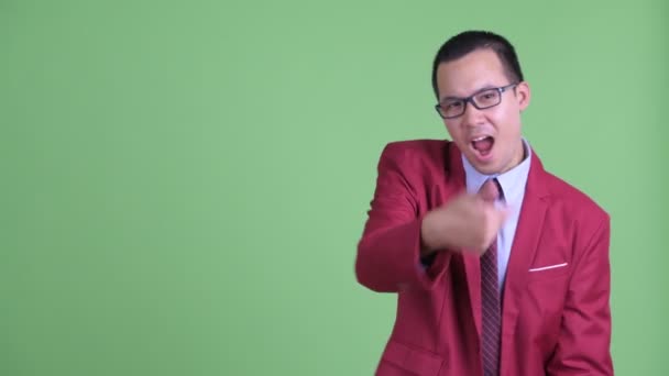 Boldog ázsiai üzletember szemüveg csettintő ujjakkal és mutat valamit — Stock videók