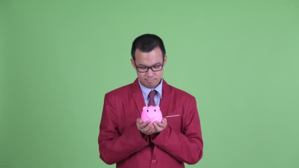 幸せなアジアのビジネスマンの顔眼鏡を保持貯金箱と見て驚き — ストック動画