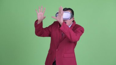 Takım elbiseli Asyalı iş adamı sanal gerçeklik kulaklığı kullanıyor ve porno izliyor.