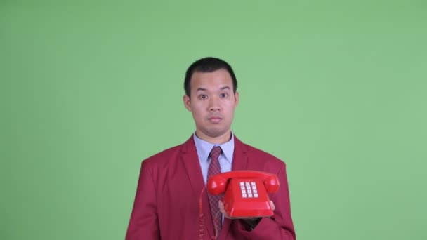 Лицо счастливого азиатского бизнесмена, пользующегося телефоном и выглядящего удивленным — стоковое видео