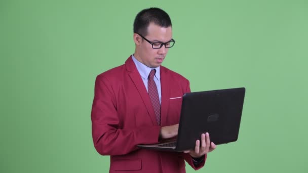 Ευτυχισμένος Ασιάτης επιχειρηματίας που μιλάει ενώ χρησιμοποιεί φορητό υπολογιστή — Αρχείο Βίντεο