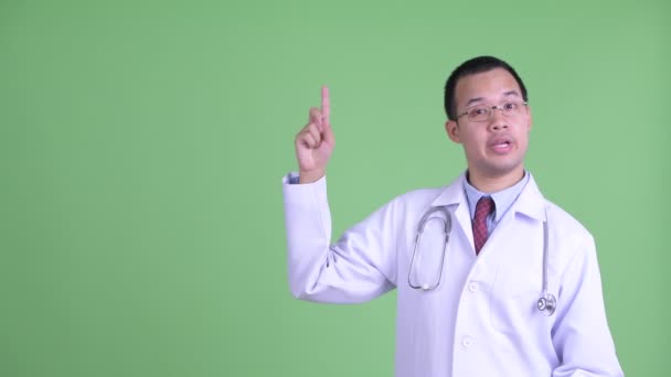 Boldog ázsiai férfi orvos beszél, miközben felfelé mutat — Stock videók