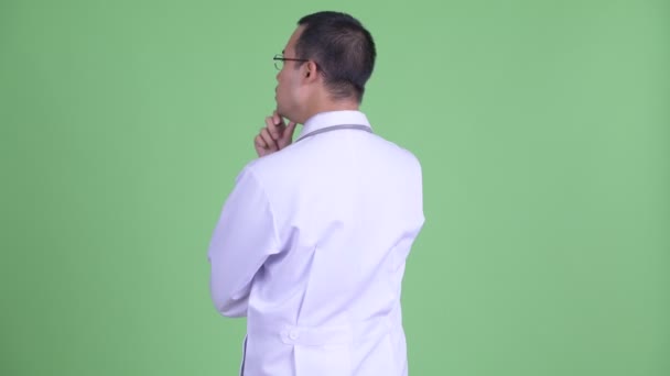 Bakifrån av asiatisk man läkare med glasögon tänker och ser sig omkring — Stockvideo