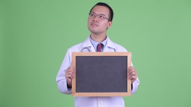Happy Asian man doctor thinking while holding blackboard — Stock Video