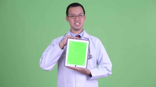 Счастливый азиатский врач говорит, показывая цифровой планшет — стоковое видео