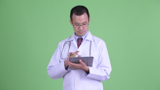 Gelukkig aziatische man arts denken tijdens het gebruik van digitale tablet — Stockvideo
