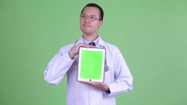 Feliz hombre asiático médico pensando mientras muestra tableta digital — Vídeos de Stock