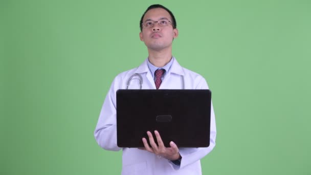 Ευτυχισμένος Ασιάτης γιατρός άνθρωπος σκέφτεται και μιλάει ενώ χρησιμοποιεί το laptop — Αρχείο Βίντεο