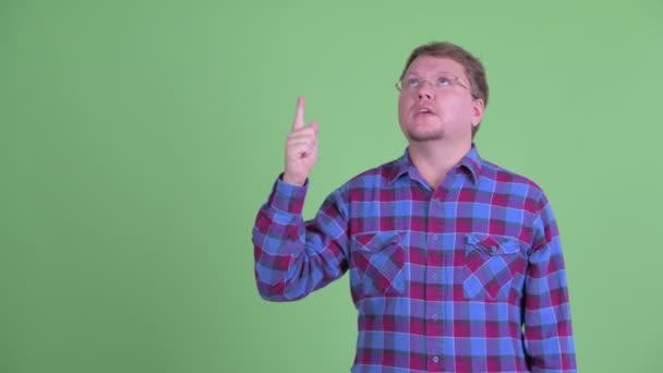 Feliz hombre hipster barbudo con sobrepeso hablando mientras señala hacia arriba — Vídeos de Stock