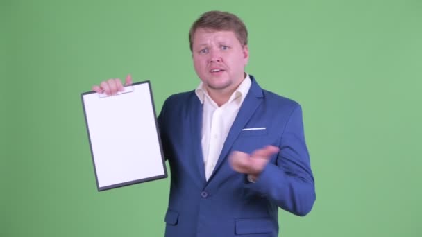 Stressed overweight bearded businessman showing clipboard and giving thumbs down — Stock Video