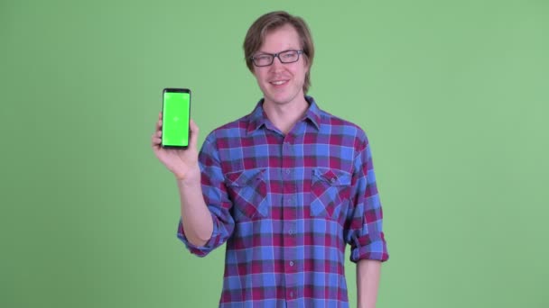 Glad ung stilig hipster man pekar och visar telefonen — Stockvideo
