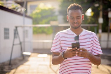 Afro saçlı, açık havada telefon kullanan mutlu bir Afrikalı.