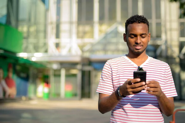 Glad ung afrikansk skäggig man använder telefon i stan utomhus — Stockfoto