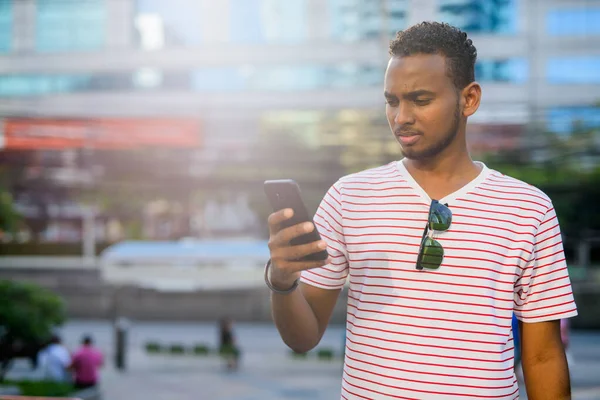 Jovem e bonito homem barbudo africano usando telefone na cidade — Fotografia de Stock