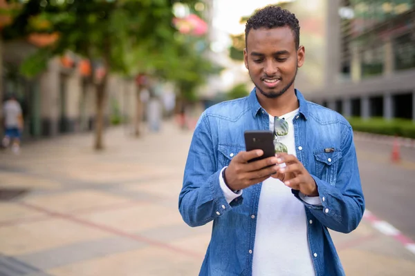 Happy young African bearded man using phone in the city streets — Stock Photo, Image