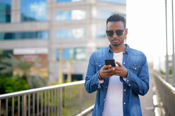 Young handsome African bearded man using phone on the footbridge — Stock Photo, Image