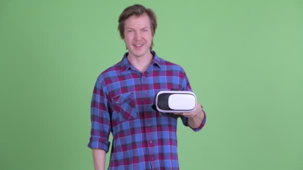 Feliz jovem hipster homem segurando e apontando para realidade virtual headset — Vídeo de Stock