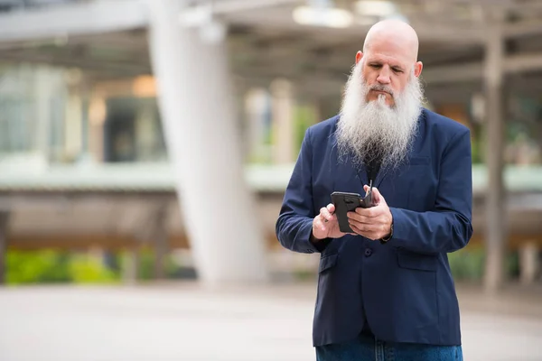 Зрілий бородатий лисий бізнесмен використовує телефон у місті на відкритому повітрі — стокове фото